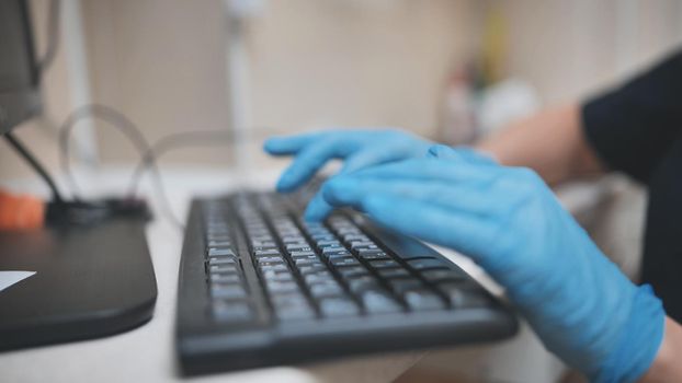 The veterinarian is typing on the keyboard in blue gloves.