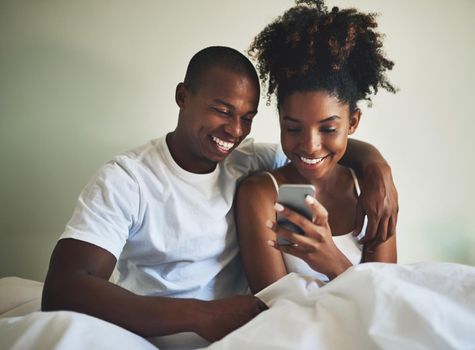 Nothing says love like a joint social media account. Shot of a happy young couple using a mobile phone together in bed at home.