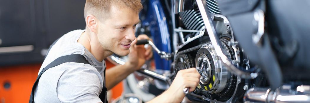 Young male locksmith disassembles motorcycle engine on bench in garage