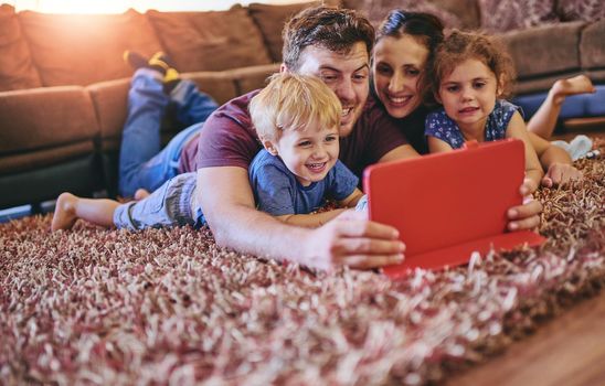 Enjoying a family-friendly movie together. Shot of a happy young family looking at a tablet together while lying on the carpet in their lounge.