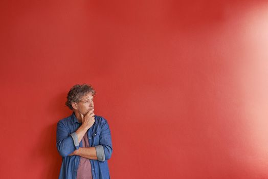 Thinking.... A mature man standing against a red background.