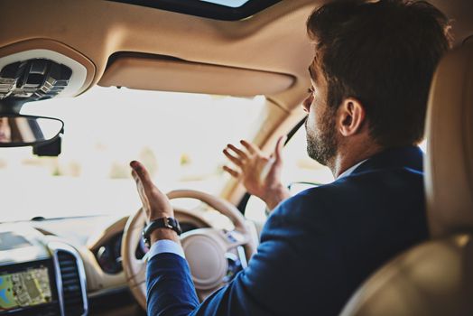 I cant believe how many cars are on the road. Shot of a stressed young businessman holding up his hands in frustration while driving in his car and sitting in traffic.