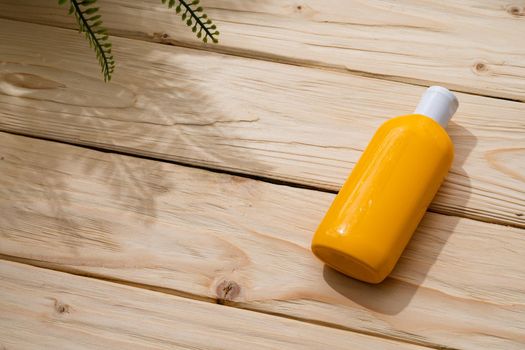 Bottle with sun protection cream on wooden background, top view