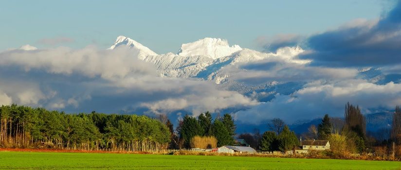 Pastoral overview over Fraser valley farm lands on snowy mountains background