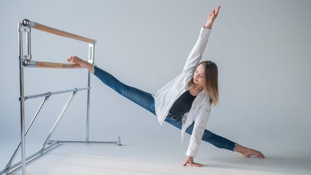 Caucasian woman in casual clothes pulls the split at the ballet barre.