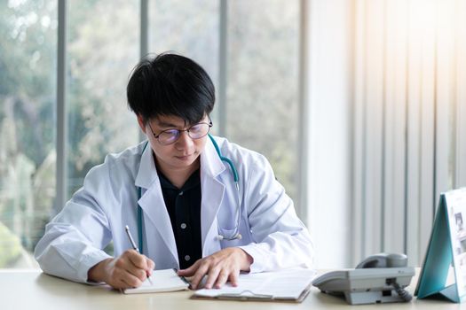 Male doctor sitting in office analyzing and writing patient sickness report