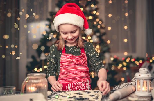 Little girl in santa hat cutting cookies