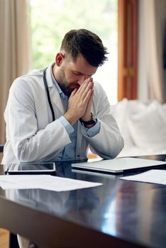 Looking for some define intervention. Cropped shot of a handsome male doctor praying while sitting in his office.