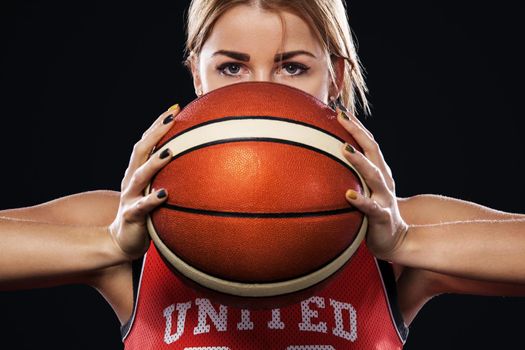 Portrait of a beautiful and woman with a basketball in studio. Sport concept on black background.