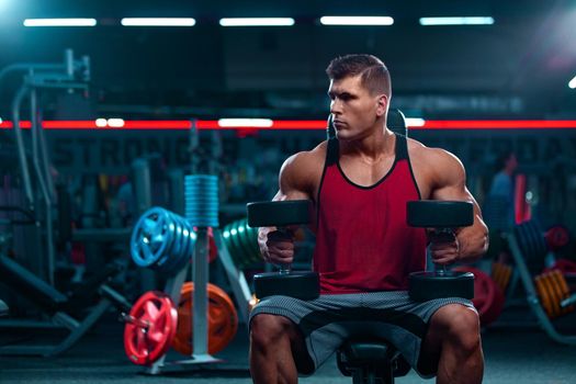 Bodybuilder athlete man with dumbbells pumping up muscles in the gym. Brutal strong muscular guy on fitness workout. Bodybuilding concept.