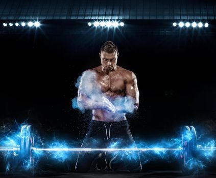 Photo of strong muscular bodybuilder athletic man pumping up muscles with barbell on black background with lights. Workout energy bodybuilding concept.