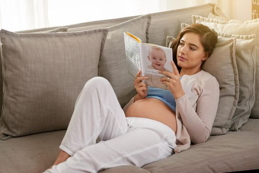 Researching the A to Zs of pregnancy, childbirth and parenting. Shot of a young pregnant woman reading a baby book at home.