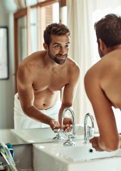 Getting a fresh start to the day. Shot of a happy shirtless man rinsing his face by the bathroom sink.