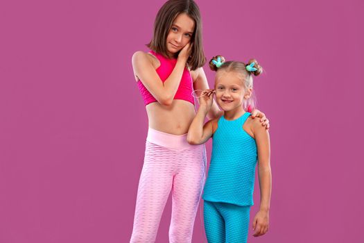 Two children girls listen to music on a pink background. Kids lifestyle concept.
