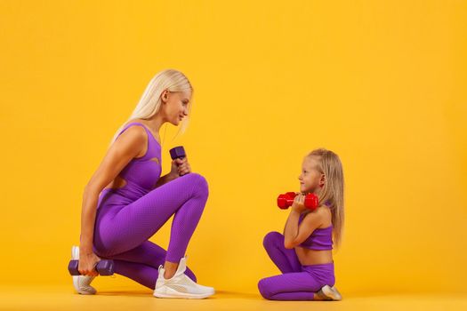 Mother's day concept. Young mother and daughter exercise together with dumbbells. Family look.