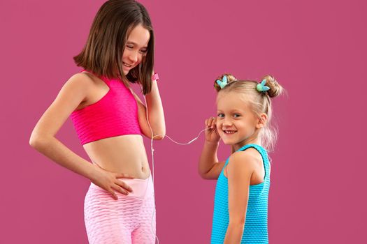 Two children girls listen to music on a pink background. Kids lifestyle concept.