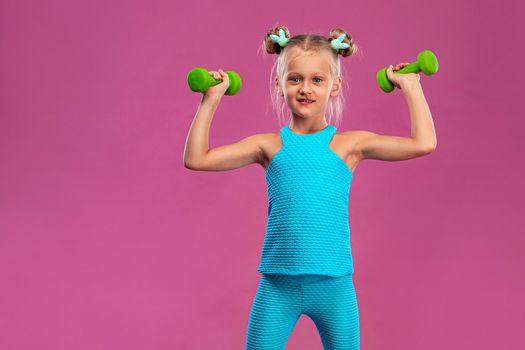 Kid girl doing fitness or yoga exercises with dumbbells isolated on pink background