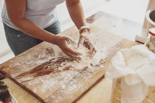 Housewife kneads flour dough on a wooden board against the background of the kitchen