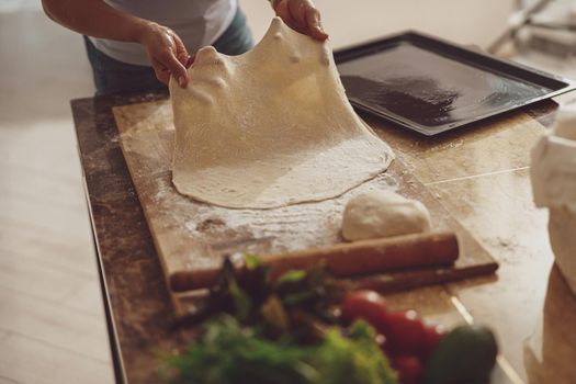 Housewife rolls out pizza dough on a wooden board to spread on a baking sheet