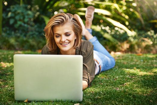 She blogs every chance she gets. Shot of an attractive young woman using her laptop while outside on the grass.