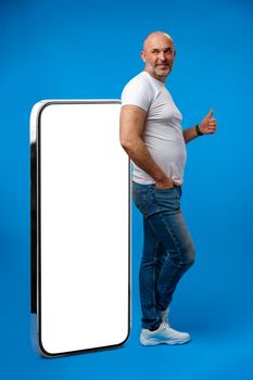 Middle-aged man standing and showing big smartphone with blank white screen
