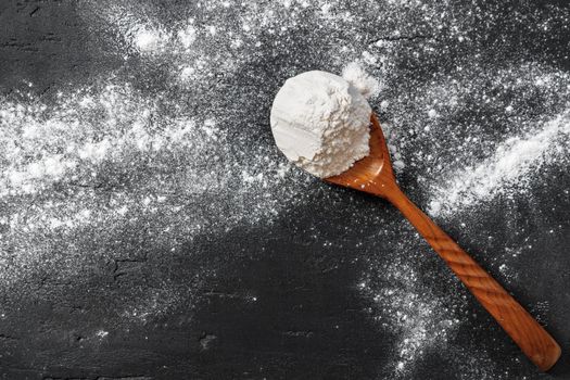 Pile of flour in wooden spoon on dark background