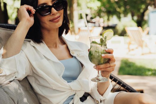Young Brunette Woman Relaxing and Drinking Cocktail While Sitting on Restaurant Terrace Outdoors in Summer Sunny Day