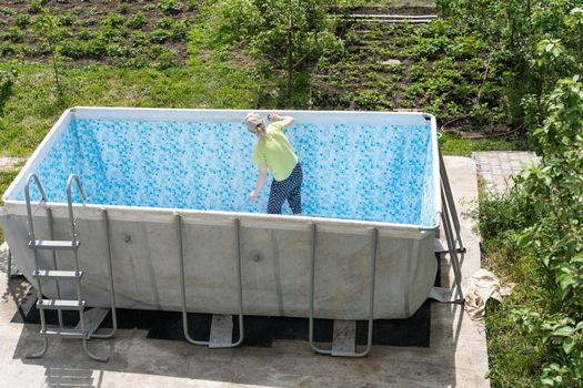 woman cleans the empty pool in the yard against the background of nature.