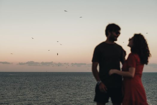 Unfocused Blurred Couple Standing on the Background of Sea After Sunset at Evening, Seagulls Flying Over Water