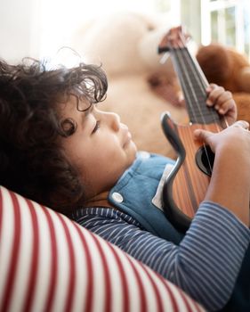 Strumming for dreams. Shot of an adorable young boy playing with a guitar in his bedroom at home.