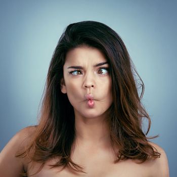 Beauty begins when you decide to be yourself. Studio shot of a beautiful young woman making a silly face against a blue background.