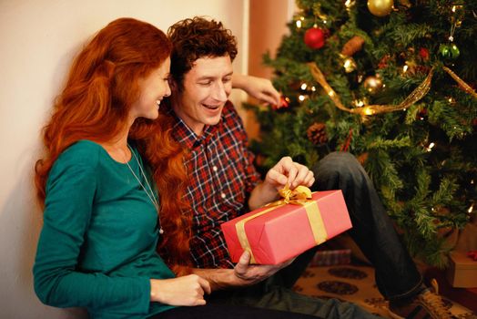 Sharing Christmas with someone special. Shot of a young man opening his christmas present while sitting with his girlfriend.