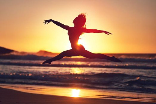 Take a risk. Silhouette of an energetic woman jumping on the beach at sunset.
