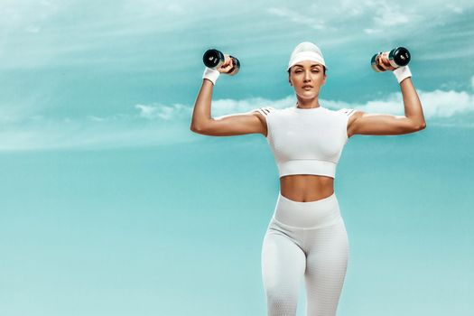 Sporty and fit woman athlete doing training with dumbbells on the sky background. The concept of a healthy lifestyle and sport. Individual sports recreation.