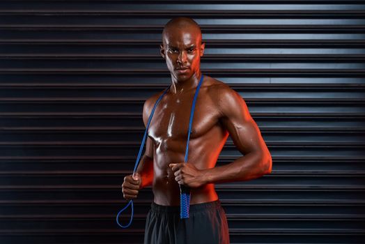 Time to do some cardio. Studio shot of an athletic young man holding a skipping rope around his shoulders against a grey background.