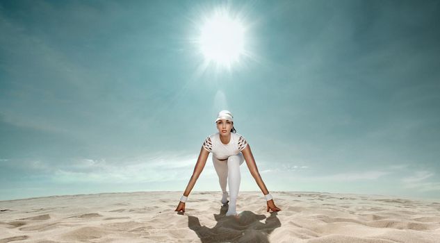 Strong athletic woman sprinter, start running at the desert wearing in white sportswear. Fitness and sport motivation. Runner concept with copy space.