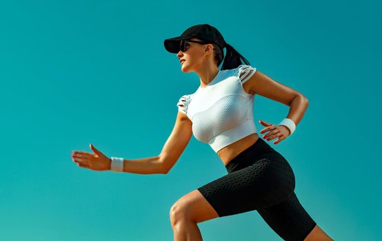 Sporty young woman and fit athlete runner running on the sky background. The concept of a healthy lifestyle and sport. Woman in black and white sportswear.
