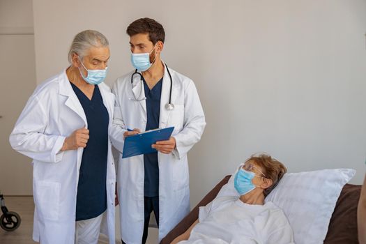 Professional doctors in mask discuss over patient's diagnosis standing in hospital ward
