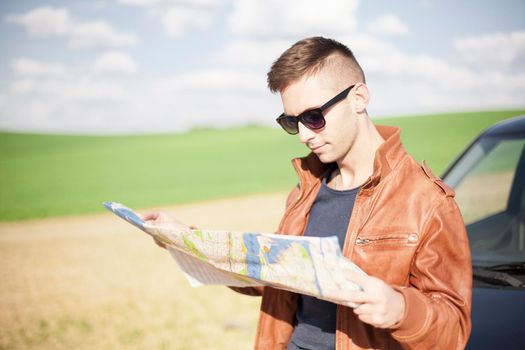 A tourist man next to the car looks at the map of the area. Traveler