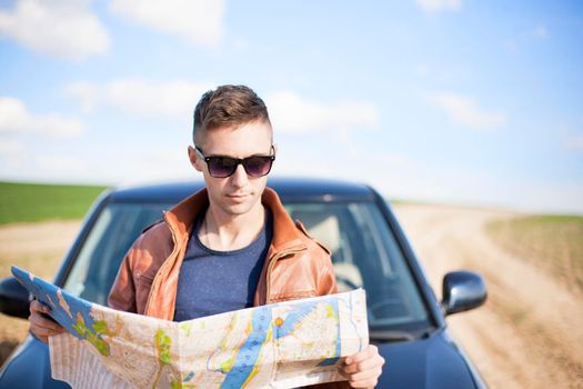 A tourist man next to the car looks at the map of the area. Traveler