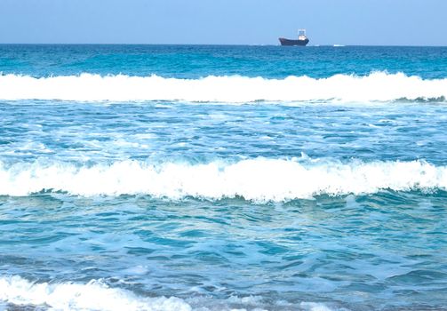 three waves near the shore. a blurred ship on the horizon