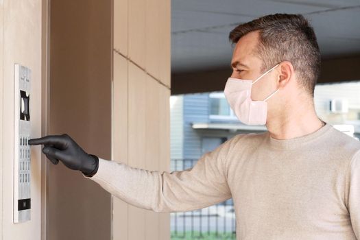 Man in face mask and gloves dials the code on the intercom and going in porch of his apartment. Pandemic covid-19 concept