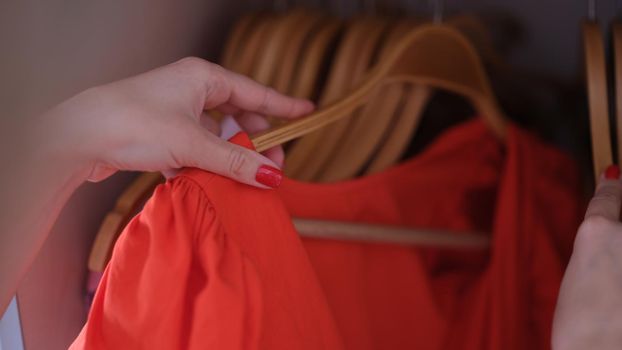 Female hand choosing red dress on hanger closet closeup