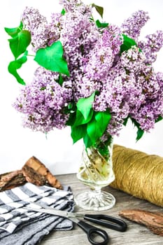 Lilac spring bouquet in glass vase on table with scissors and rope