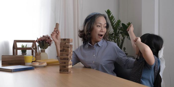 Happy moments of Asian grandmother with her granddaughter playing jenga constructor. Leisure activities for children at home.