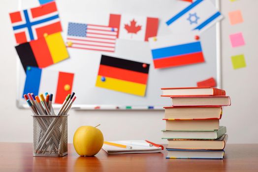 Stack of books, pencils, an apple in front of school whiteboard with flags of different countries