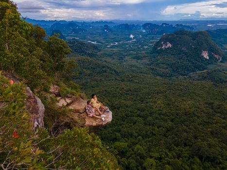 Dragon Crest mountain Krabi Thailand, a Young traveler sits on a rock that overhangs the abyss, with a beautiful landscape. Dragon Crest or Khuan Sai at Khao Ngon Nak Nature Trail