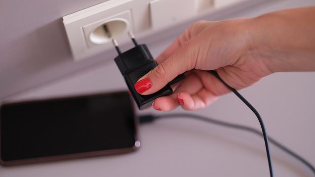 Woman hand plugging mobile phone charger into socket closeup