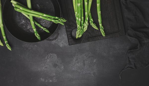 Fresh green asparagus in a round cast iron pan on a black table