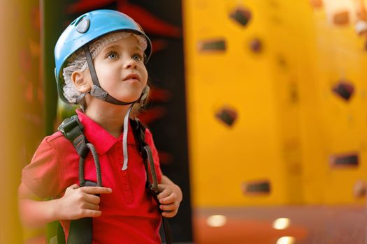Cute little girl climber in blue protective helmet and gear for climbing standing in climber centre amusement park for children